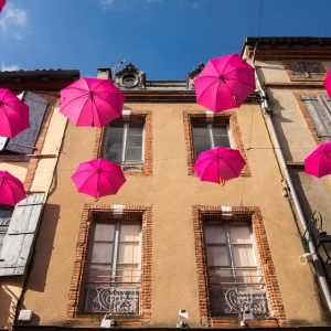 Jakobsweg Moissac rosa Oktober Regenschirme vor Fassade sonnig