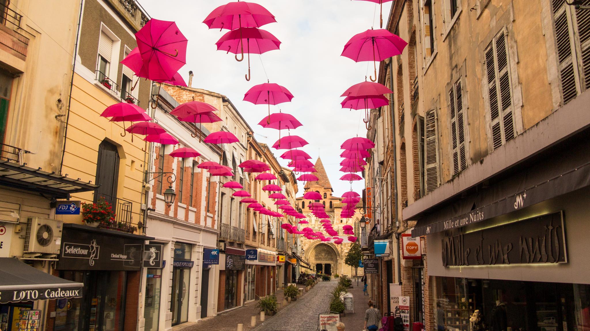 Jakobsweg Moissac rosa Oktober Regenschirme entlang der Straße mit Kirche